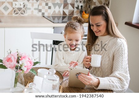 Smiling mother takes selfie with cute daughter on tablet, happy young mom laughing makes photo with daughter at home, single mom and adopted children playing fun with phone