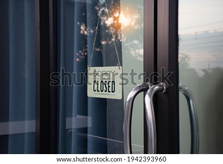 The board hung in front of the glass door of the coffee shop had a message sorry and closed. Light from the soft sun in the morning was bright as the background. Reflection from nature, sky, trees
