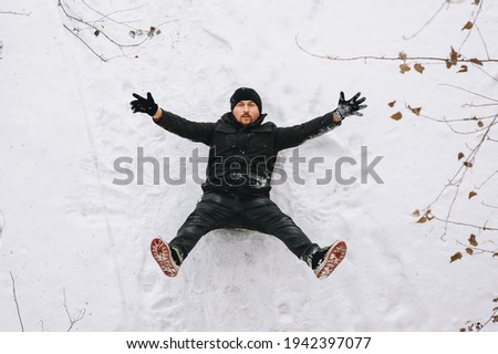 A cheerful, brave man in black clothes falls from a great height onto white snow in winter and expresses emotions. Photography, concept.