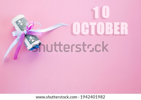 calendar date on pink background with rolled up dollar bills pinned by pink and blue ribbon with copy space. October 10 is the tenth day of the month.