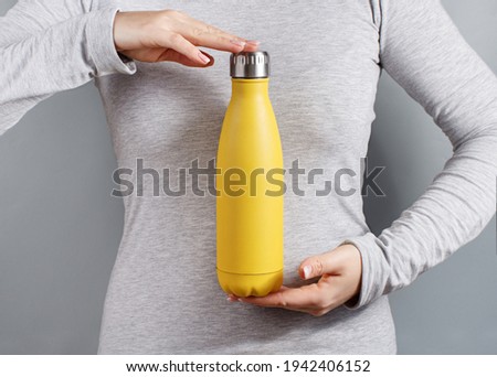 Close up of woman in grey tee holding yellow insulated bottle on grey background