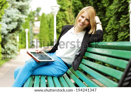 Smiling woman sitting on the bench with tablet computer