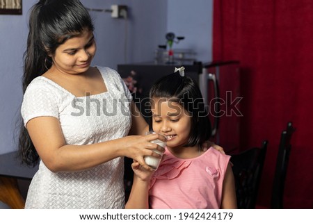 An Indian Asian mother giving glass of milk to her daughter