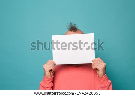 Bearded european man in casual peach isolated on turquoise background holding white empty paper board 