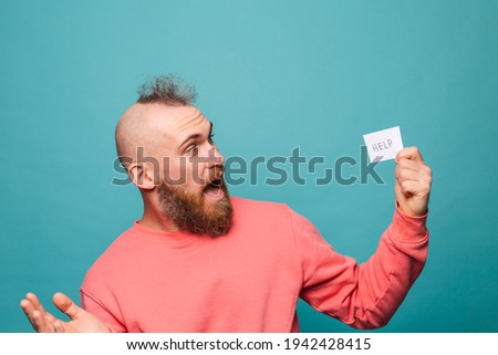 Bearded european man in casual peach isolated on turquoise background holding paper with help sign brutal shocked surprised