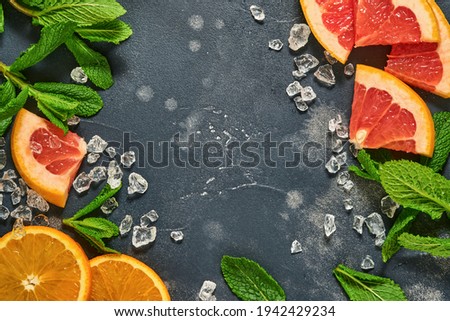 Grapefruit and orange slices, mint, cane sugar, ice, cocktail tubes, juicer or squeezer on black stone old background. Ingredients for making summer beach cocktail drink background. Mock up. Top view.
