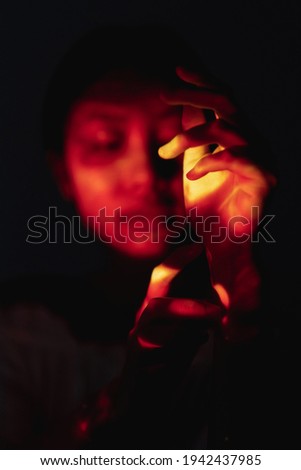 Spiritual ritual. Sacred ceremony. Tribal healing. Ethnic culture. Mistic native Indian shaman woman face silhouette with hand in red orange light isolated on defocused black night background.