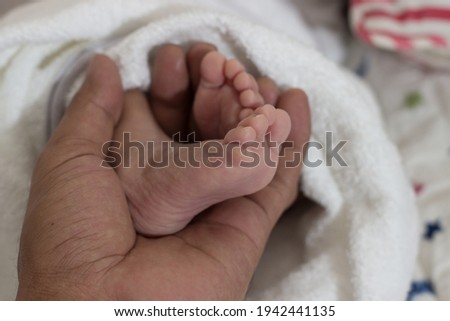 Close up newborn baby's tender feet, hand holding legs of the baby. Adorable softness of feet, toes and nails for health and medical uses of illustration, and its connection of parents to the baby. 