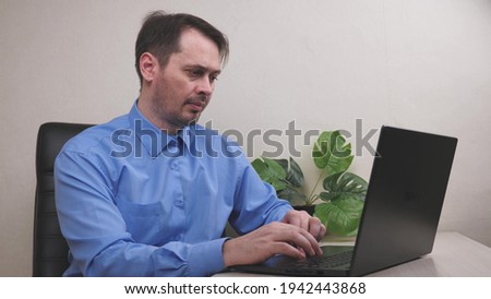 A serious man works at a laptop in the office, an employee conducts a business on a computer, a freelancer types important documents on a keyboard, payments for receipts online via the Internet