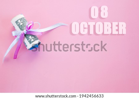 calendar date on pink background with rolled up dollar bills pinned by pink and blue ribbon with copy space. October 8 is the eighth day of the month.