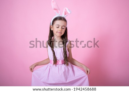 Little girl with Easter bunny ears posing on a studio pink background copy space. Easter holiday concept.