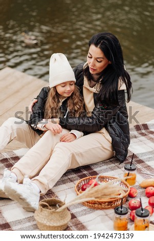 beautiful brunette mom and her daughter on a picnic near the lake in the autumn park