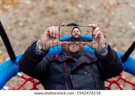 Man taking selfie with smartphone while resting on swing outdoors