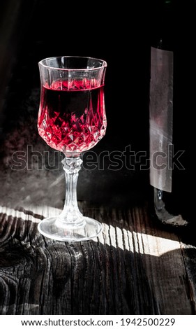 Red wine in a wine glass illuminated by side light in a dark area.Wine and wine bottle on a wooden floor.
