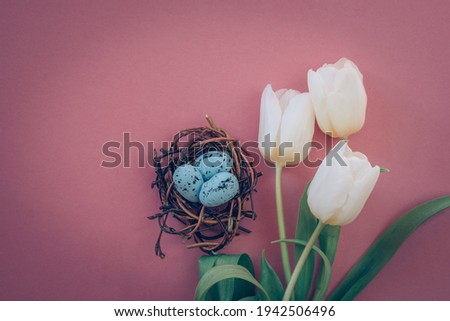 colorful easter eggs in nest and white tulip flowers against pink background