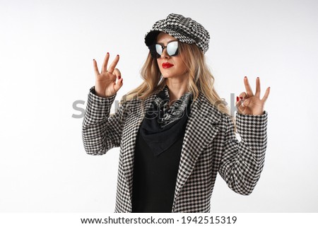 A beautiful woman in a black and white plaid dress, sunglasses, making signs with her hands.