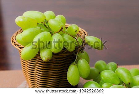 Green Grape placed in a woven basket and a wooden table top.