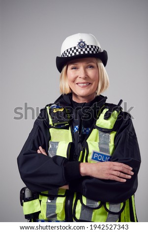 Studio Portrait Of Smiling Mature Female Police Officer Against Plain Background