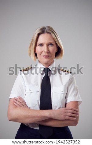 Studio Portrait Of Smiling Mature Female Airline Pilot Against Plain Background Royalty-Free Stock Photo #1942527352