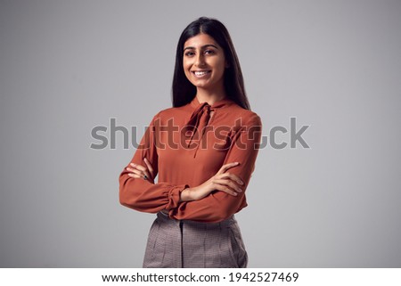 Studio Portrait Of Smiling Young Businesswoman With Folded Arms Against Plain Background Royalty-Free Stock Photo #1942527469