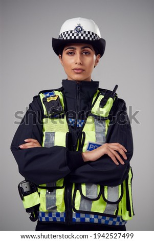 Studio Portrait Of Serious Young Female Police Officer Against Plain Background