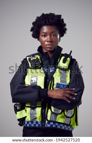 Studio Portrait Of Serious Young Female Police Officer Against Plain Background