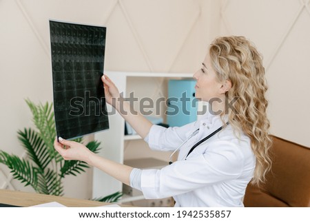 Concept of healthcare, treatment plan and rehabilitation after injury. Woman doctor in white coat look at x-ray picture. GP work in private clinic, checking magnetic resonance imaging of the brain