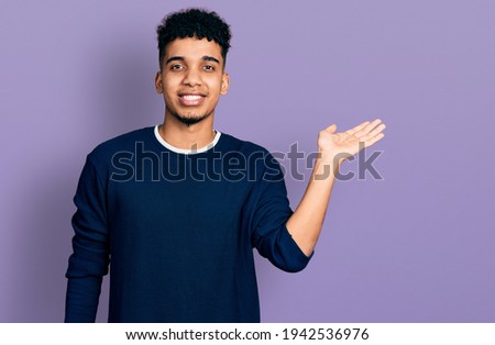 Young african american man wearing casual clothes smiling cheerful presenting and pointing with palm of hand looking at the camera. 