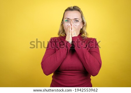 Young caucasian woman wearing casual red t-shirt over yellow background shocked covering mouth with hands for mistake. secret concept.