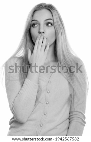 Studio shot of young beautiful teenage girl covering mouth while looking shocked