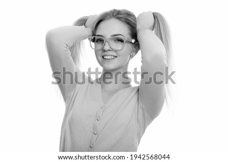 Studio shot of young happy teenage girl smiling while playing with her hair to pigtails
