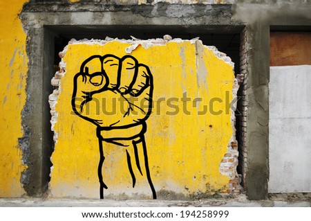 Graffiti print of a punching fist on a broken yellow wall of a demolished building.