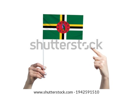 A beautiful female hand holds a Dominica flag to which she shows the finger of her other hand, isolated on white background.