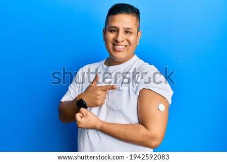 Young latin man using glucose meter button smiling happy pointing with hand and finger  Royalty-Free Stock Photo #1942592083