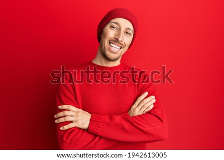Bald man with beard wearing wool sweater and winter hat happy face smiling with crossed arms looking at the camera. positive person. 