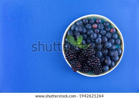 Blueberries and blackberries on a blue artisan plate with a touch of mint on a purple background.