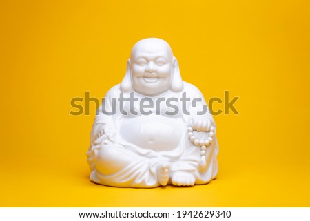 White smiling porcelain buddha statue sitting in a meditation position. Studio religious figure still life against a seamless yellow background.