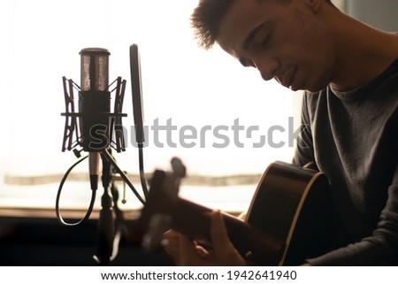 man playing spanish guitar and singing while recording it with a microphone. Home studio