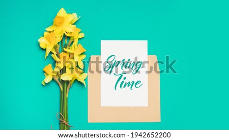 Fresh bouquet flowers of spring blossom narcissus flowers, opened craft paper envelope and white card on a green background. Spring time.