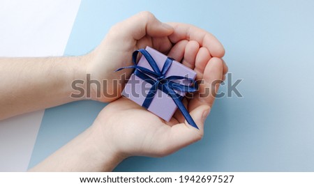 Purple gift box with blue bow in male hands on light blue background. Top view. Copy space.