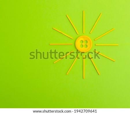 Stylized Yellow sun made from button and wood sticks on a green background. Creative spring flat lay.