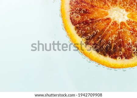 Slice of red orange submerged in mineral water surrounded with bubbles on a light blue background. Close up.
