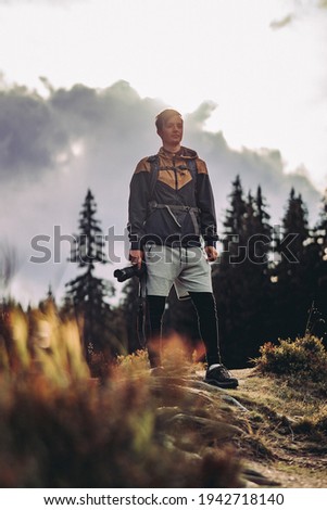 Selfie of a beginning photographer in sportswear at sunset in the Jizera Mountains. The man holds a camera in his hand and looks determined to do the right thing.