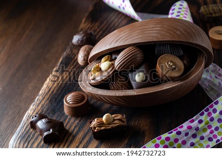 A close up of a chocolate Easter egg filled with gourmet chocolates on a wooden board. Royalty-Free Stock Photo #1942732723