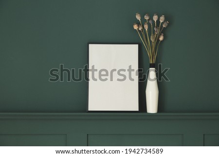 Frame mock-up and bunch of dried poppies against dark green wall.
