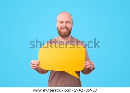 Photo of smiling young man with beard holding yellow speech bubble.