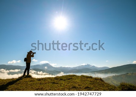 Dark silhouette of a hiker photographer taking picture of morning landscape in autumn mountains.