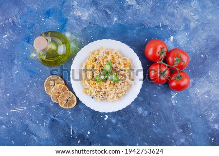 Isolated over colored blue background, red tomatoes, seared lemon slices, a glass of olive oil, green hot pepper, a white bowl with noodles. High quality photo
