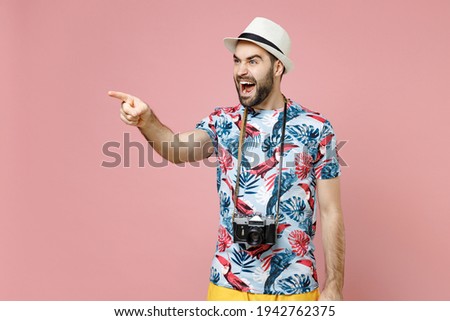 Angry young traveler tourist man in summer clothes hat with photo camera pointing index finger aside swearing isolated on pink background. Passenger traveling on weekends. Air flight journey concept