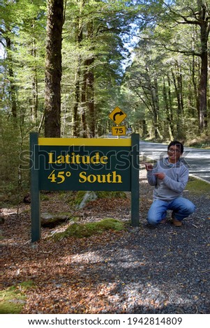 A tourist poses with the latitude 45 south signboard along the Milford Road, in Fiordland National Park.